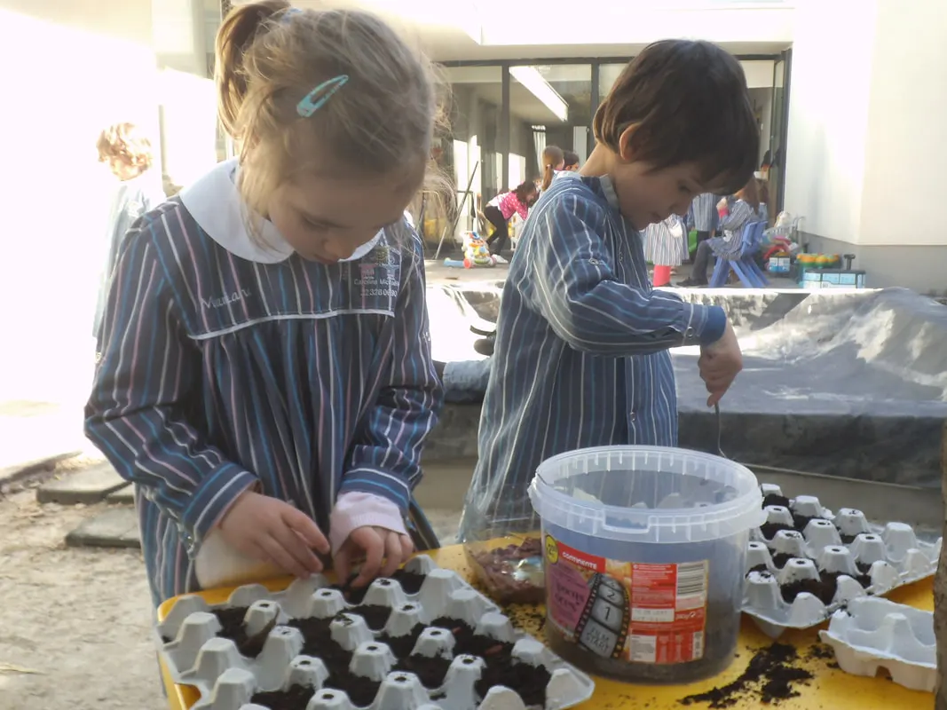 Duas meninas de bata a semear terra em caixas de ovos