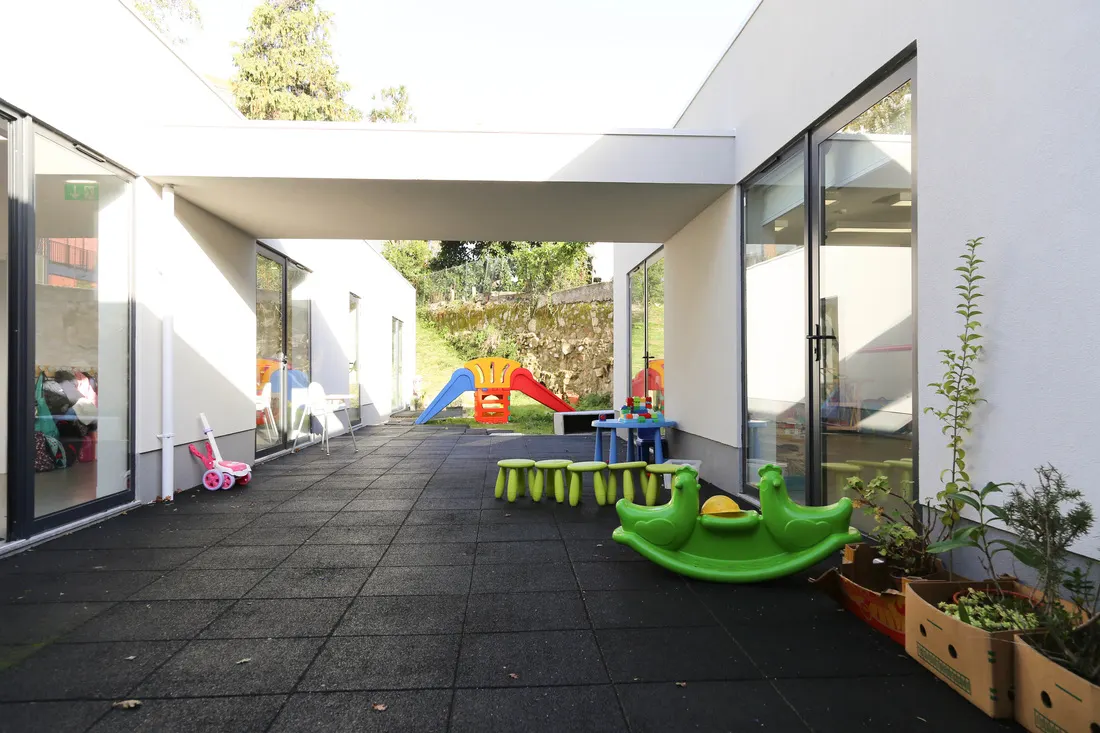 Recreio coberto com piso de borracha e brinquedos, visto da sala